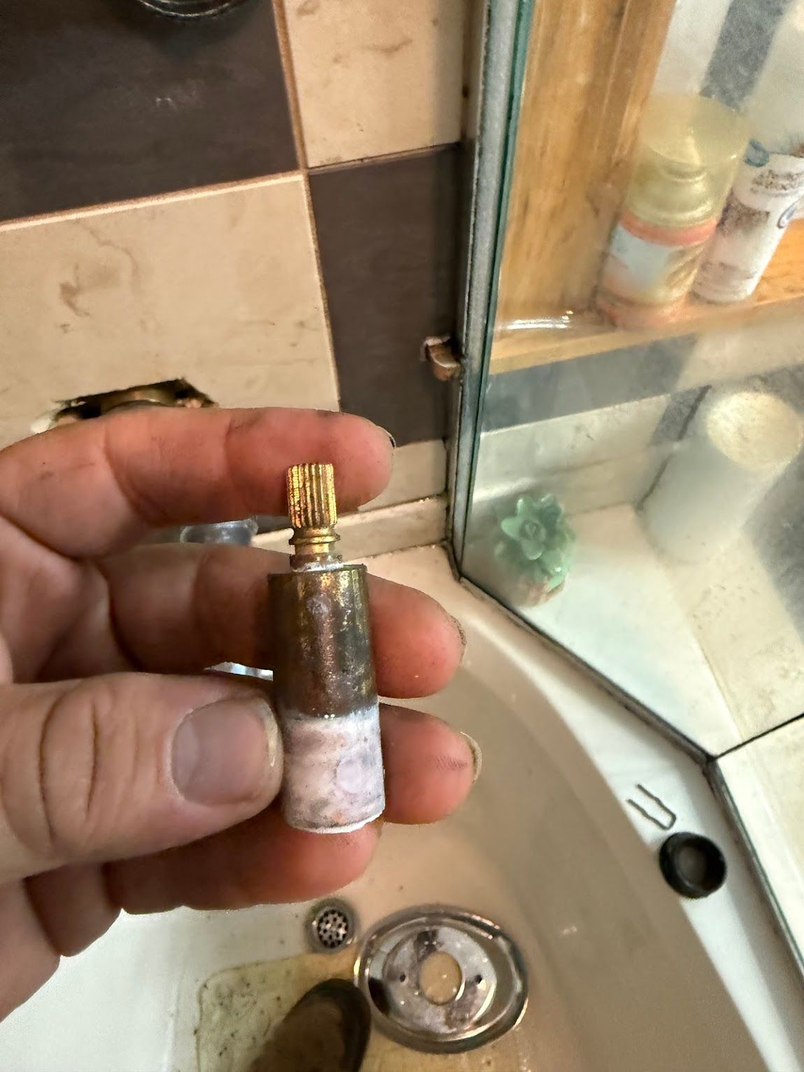 Hand holding a small rusty brass-and-metal fitting in a bathroom sink area