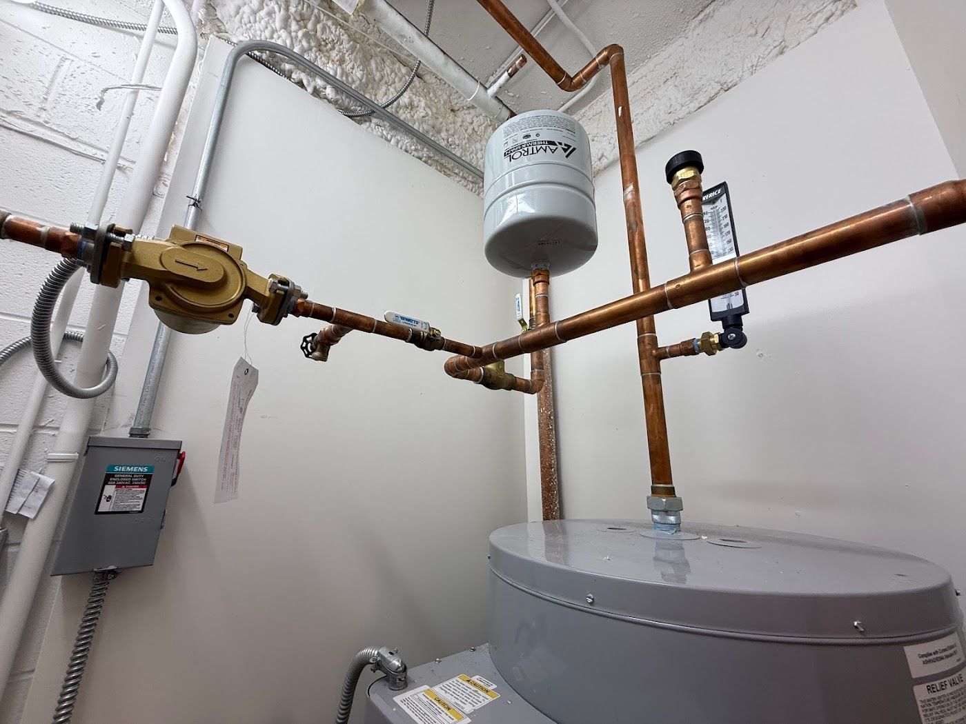 Utility room with copper pipes, valves, a wall control panel, and a large water heater.