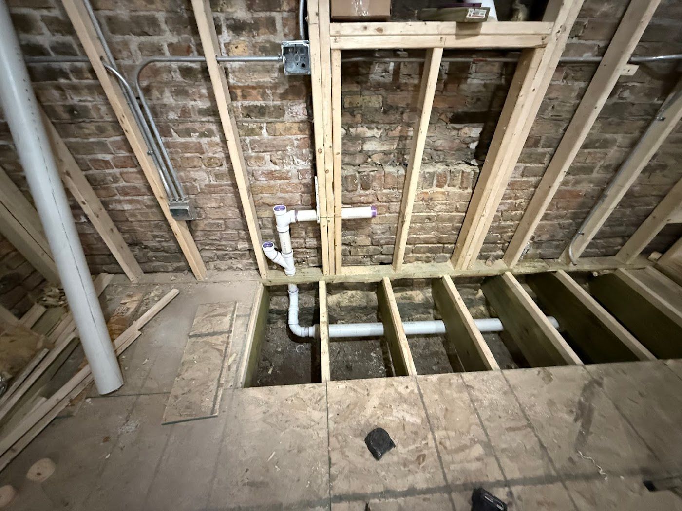 Exposed floor joists and plumbing in a partially renovated room with a large floor opening.