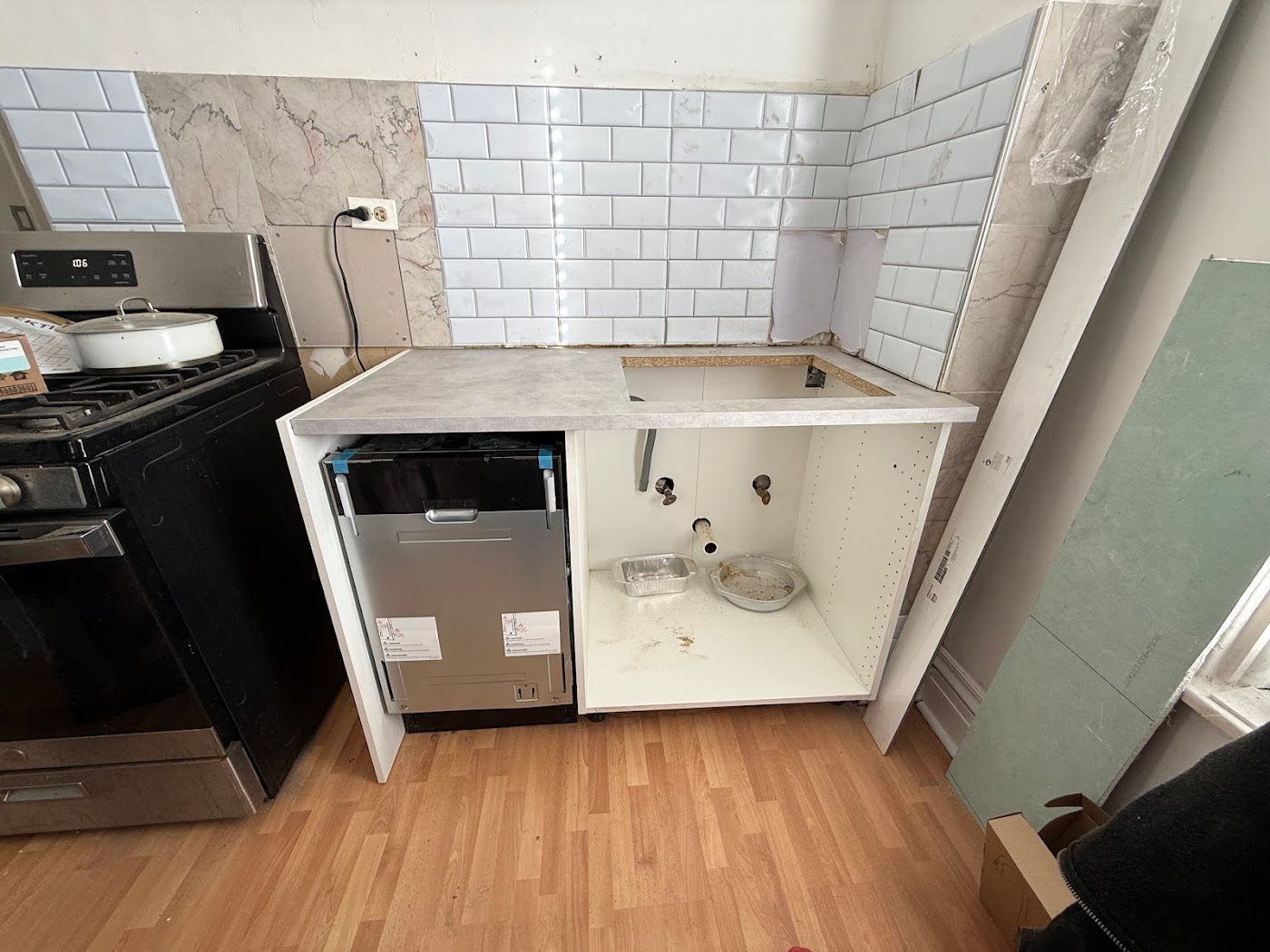 Damaged kitchen counter with a broken cabinet door, beside a stove and white tile backsplash.