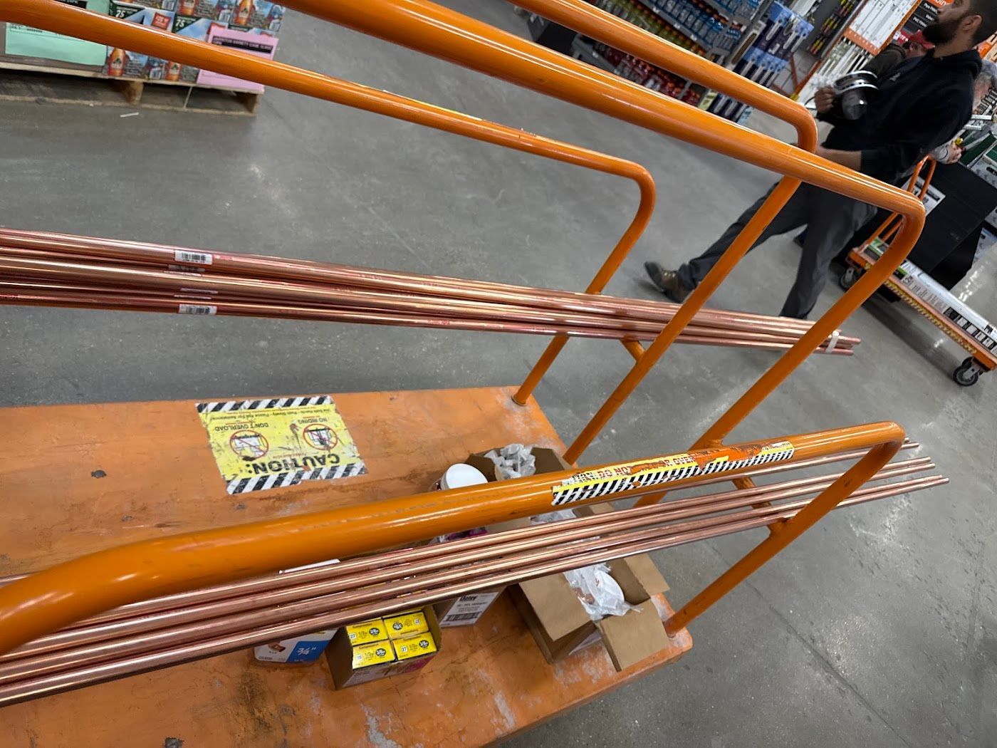 Orange metal railings and stacked materials on a warehouse floor with a worker in the background.
