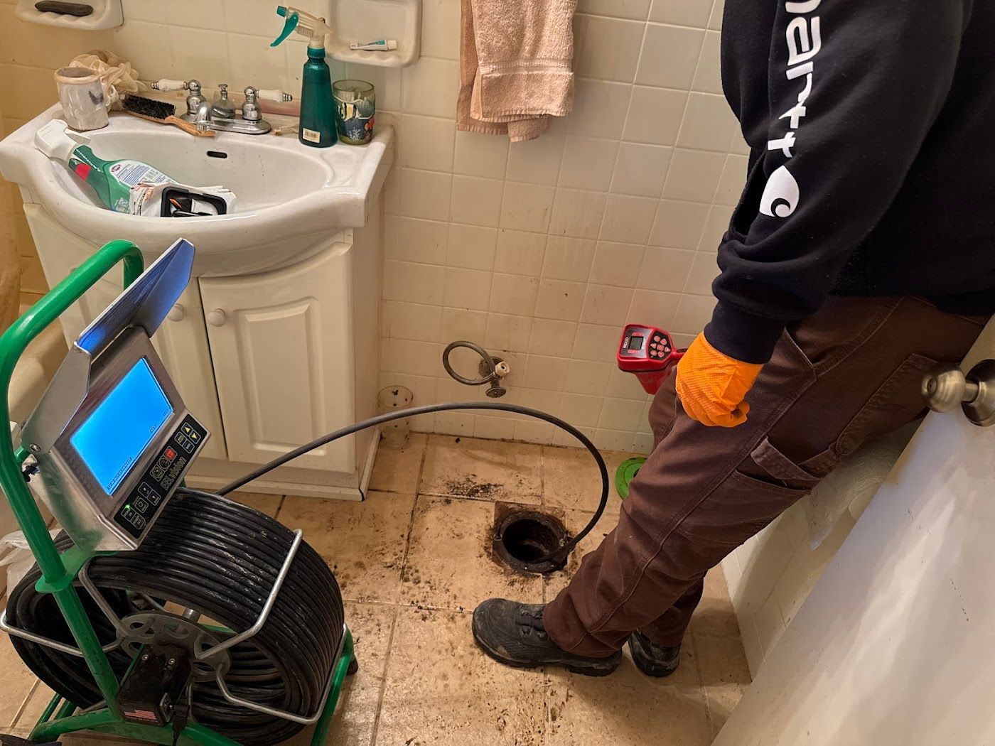 Bathroom sink with cabinet removed, exposing plumbing hole as a person inspects the floor area with a drain camera.
