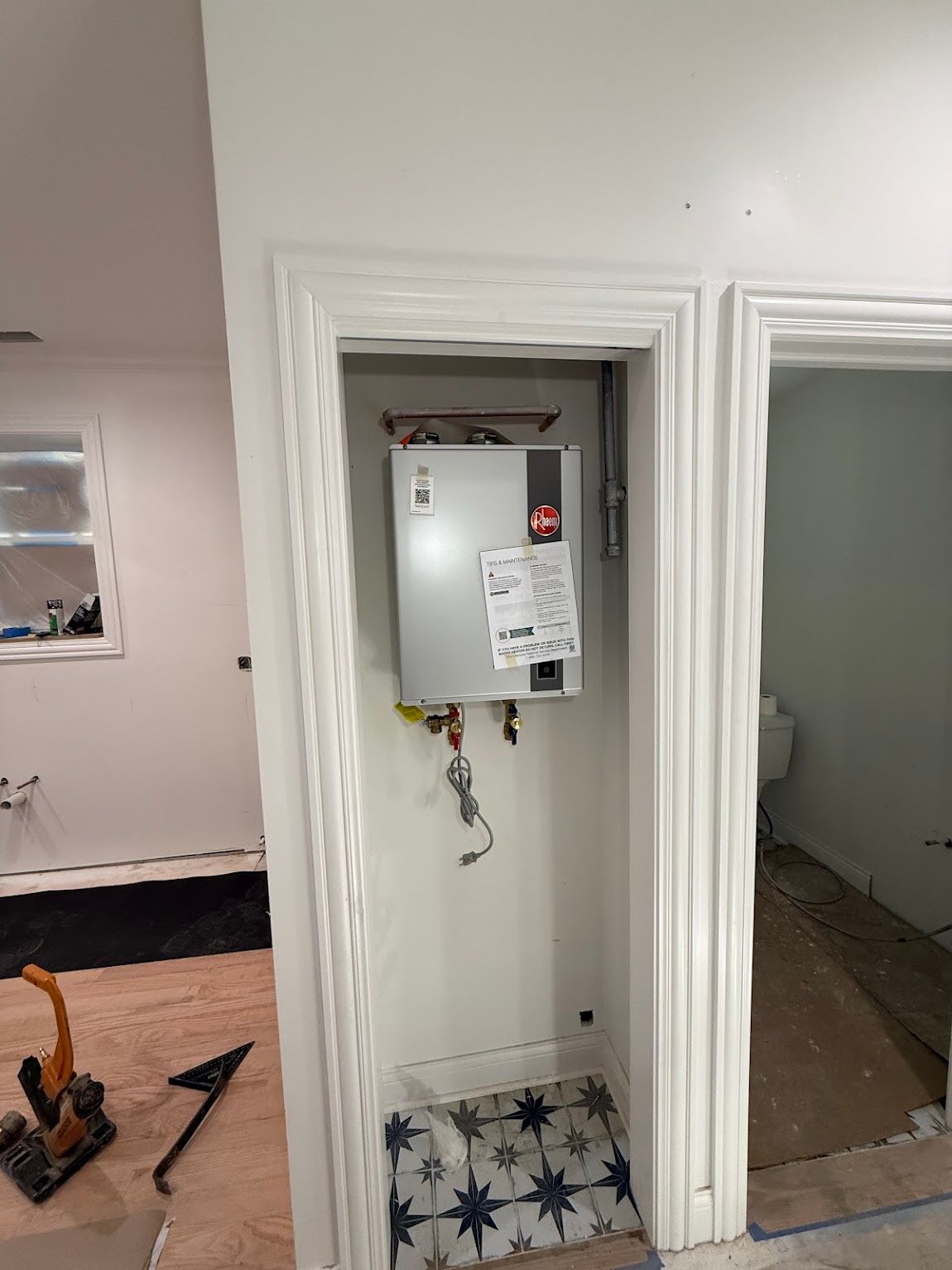 Open electrical panel in a white hallway doorway, with exposed wiring and tools on the floor nearby.