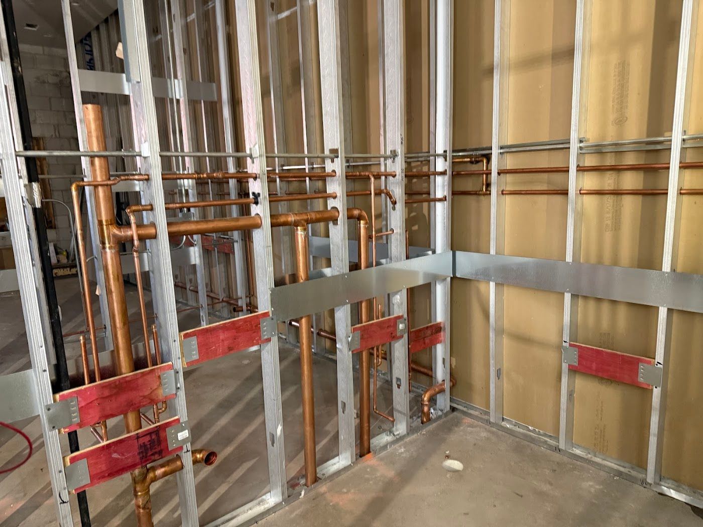 Partially framed room with metal studs, exposed pipes, and red support brackets under construction