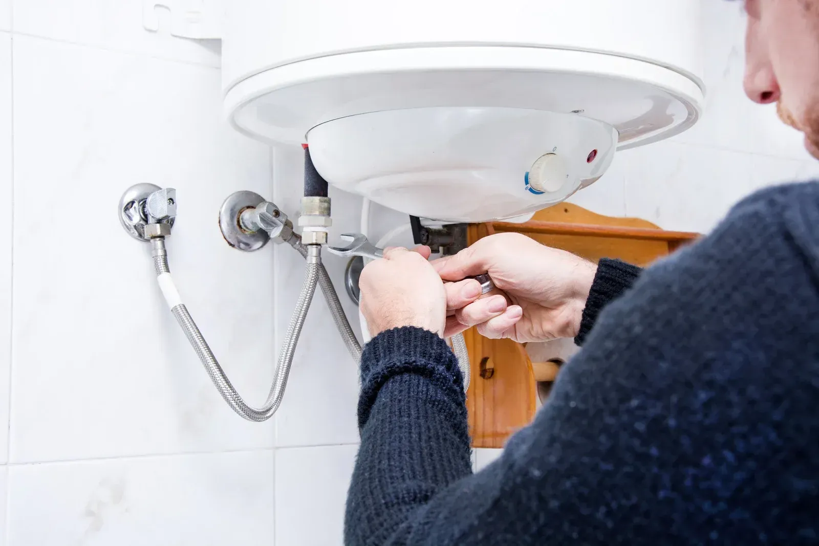 Person tightening plumbing under a bathroom sink with tools