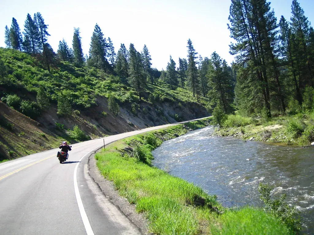 A person riding a motorcycle down a road next to a river