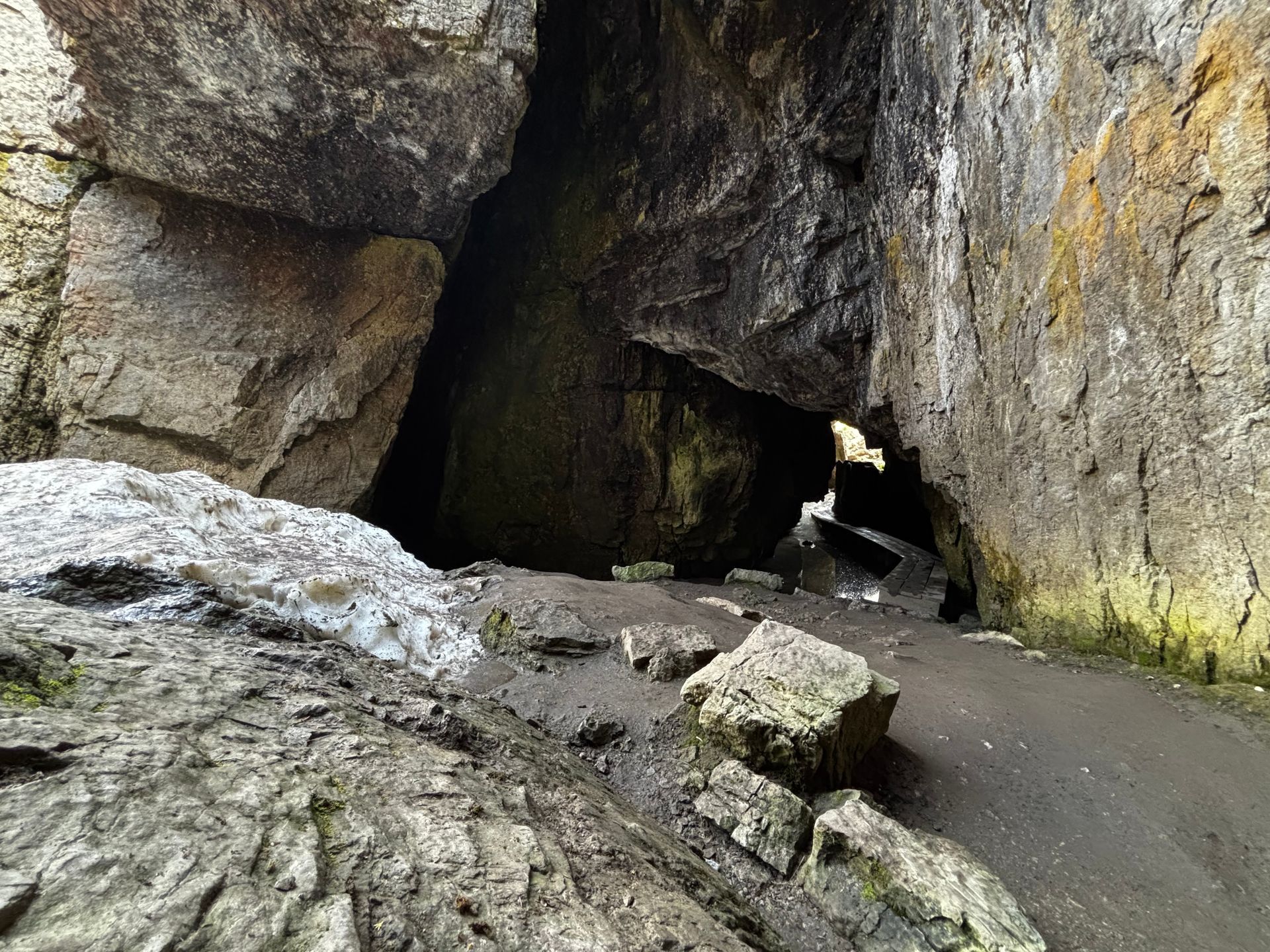 Cave entrance with large gray rocks and a dark interior.