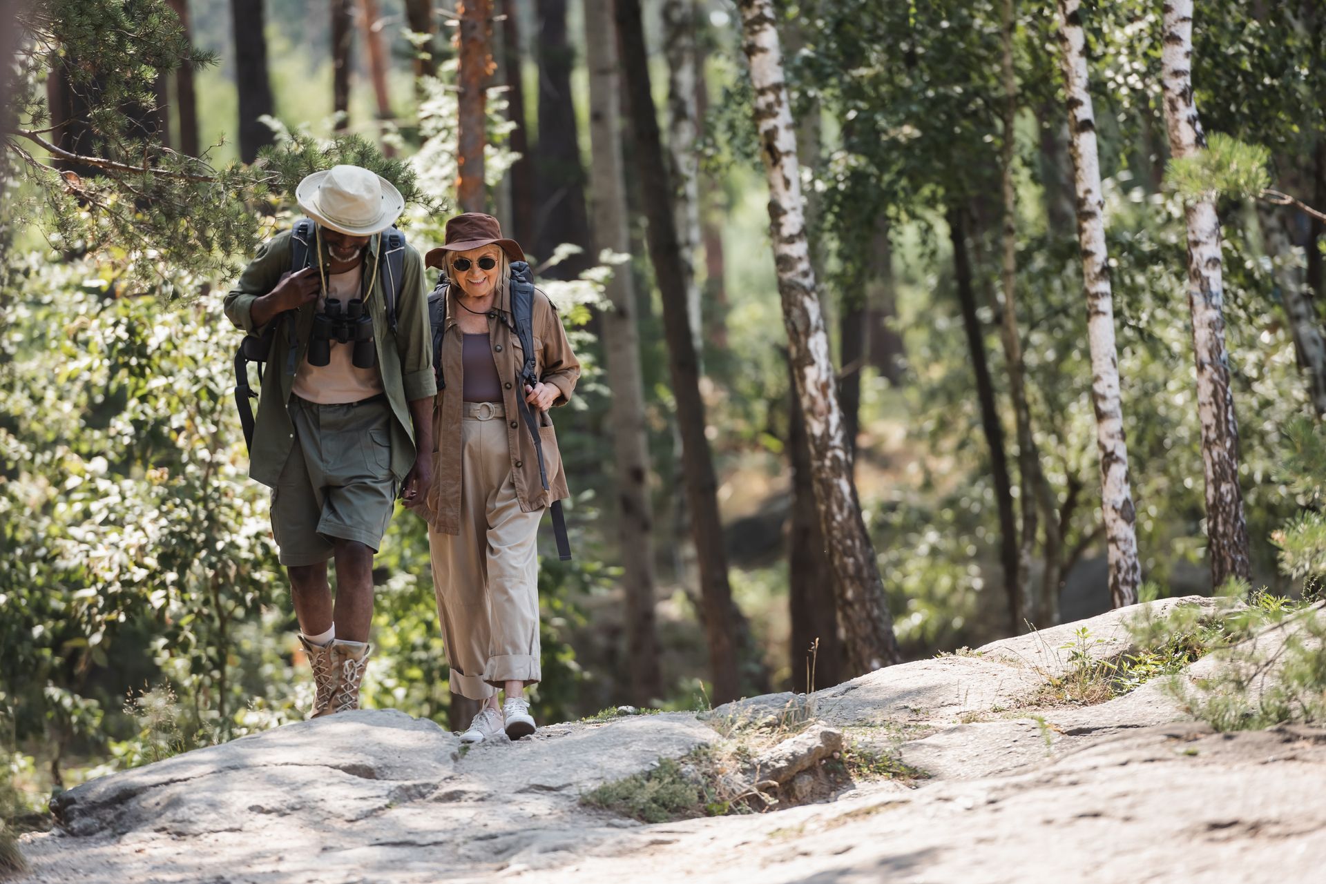 Two people hiking on a wooded trail, wearing hats and carrying backpacks.