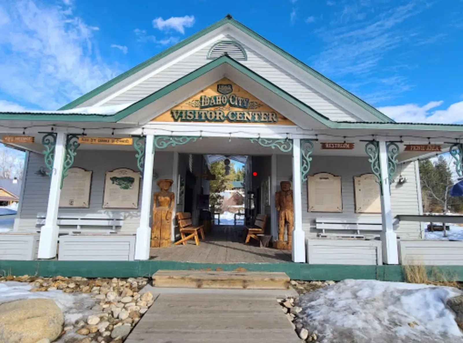 A white building with a green roof and a porch that says visitor center