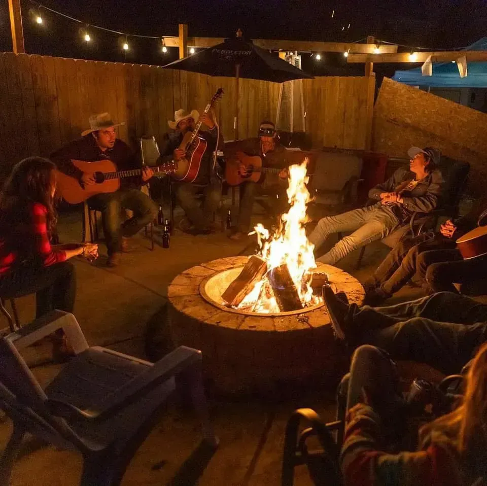 A group of people are sitting around a fire pit playing guitars