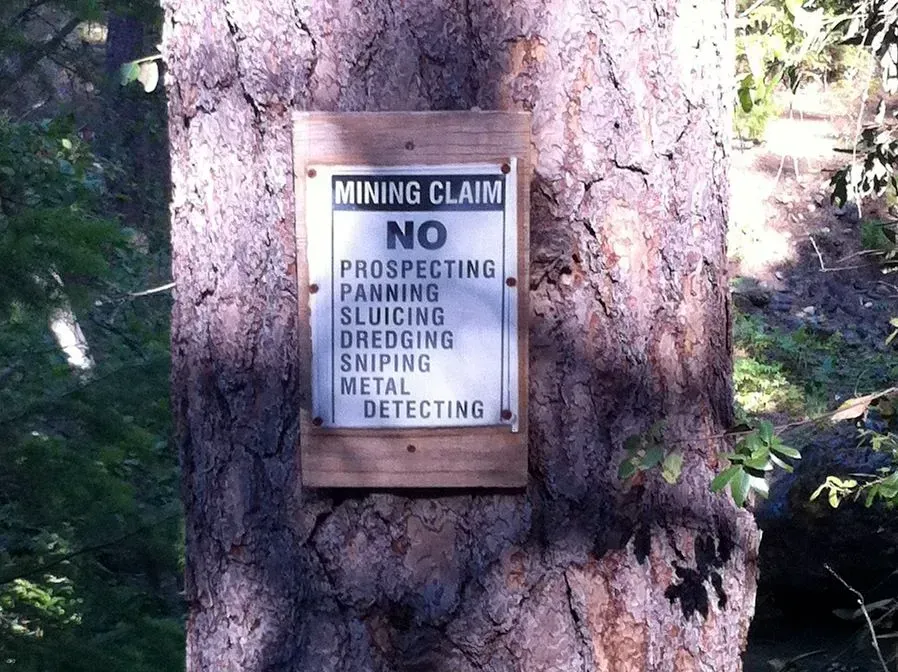 A sign on a tree says mining claim no prospecting panning sluicing dredging sniping metal detecting