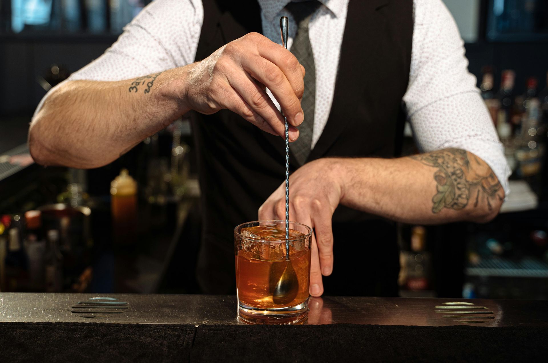 A bartender is stirring a drink in a glass with a spoon.