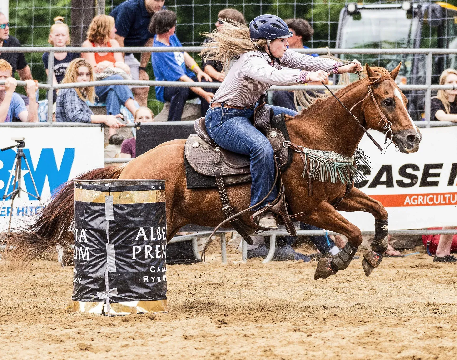 A woman is riding a horse around a barrel at a rodeo.