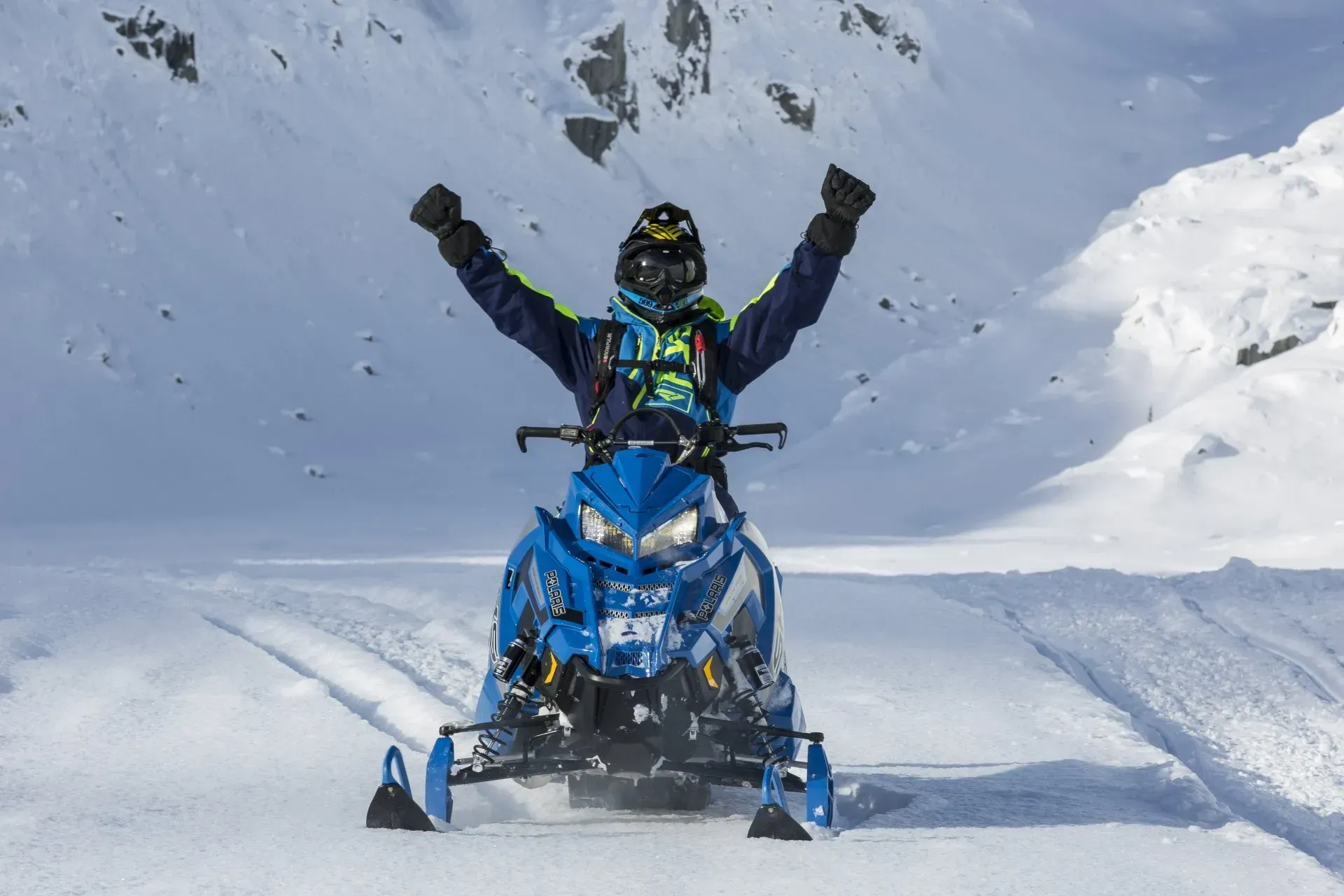 A man is riding a snowmobile in the snow with his arms in the air.