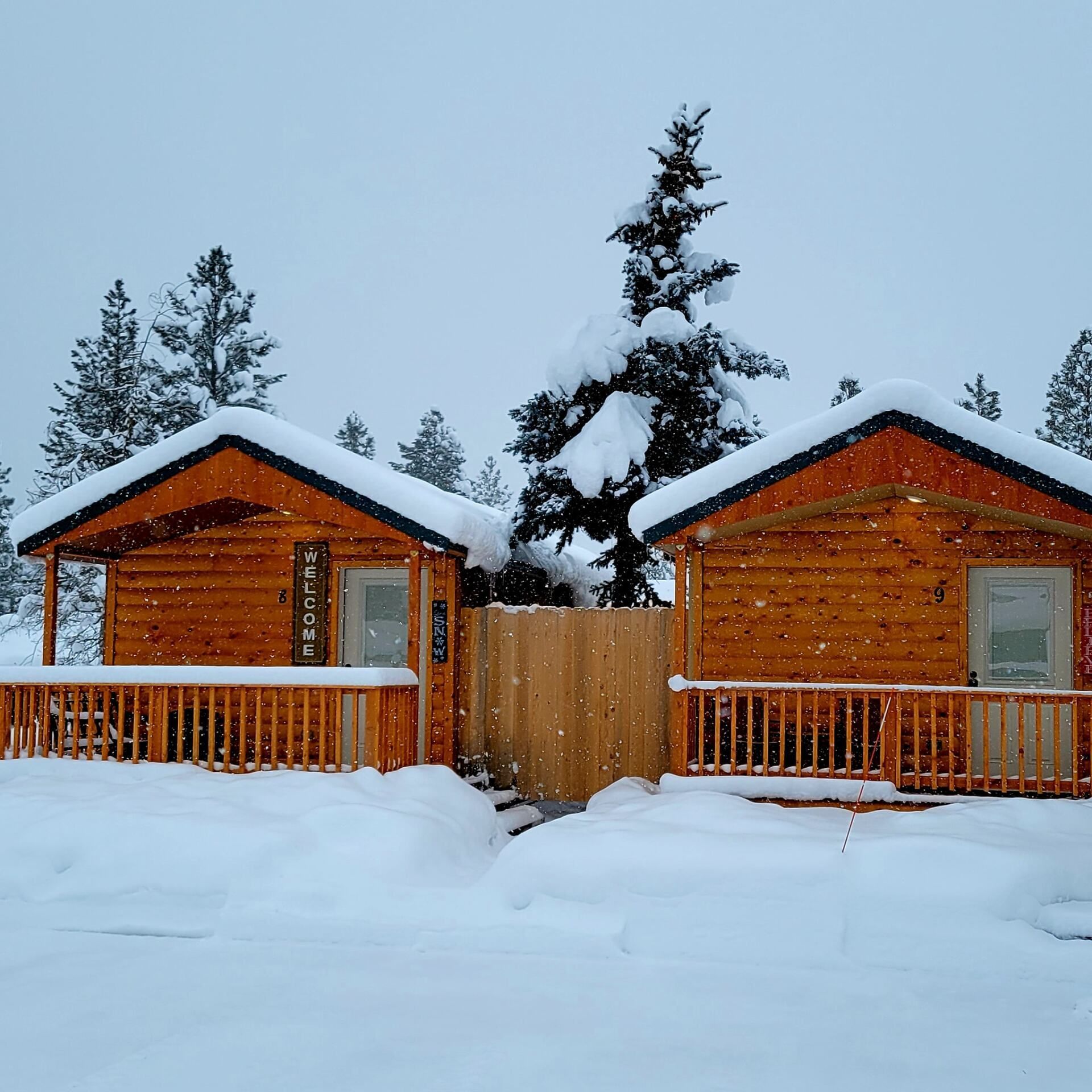 Two log cabins in the snow with a sign that says welcome