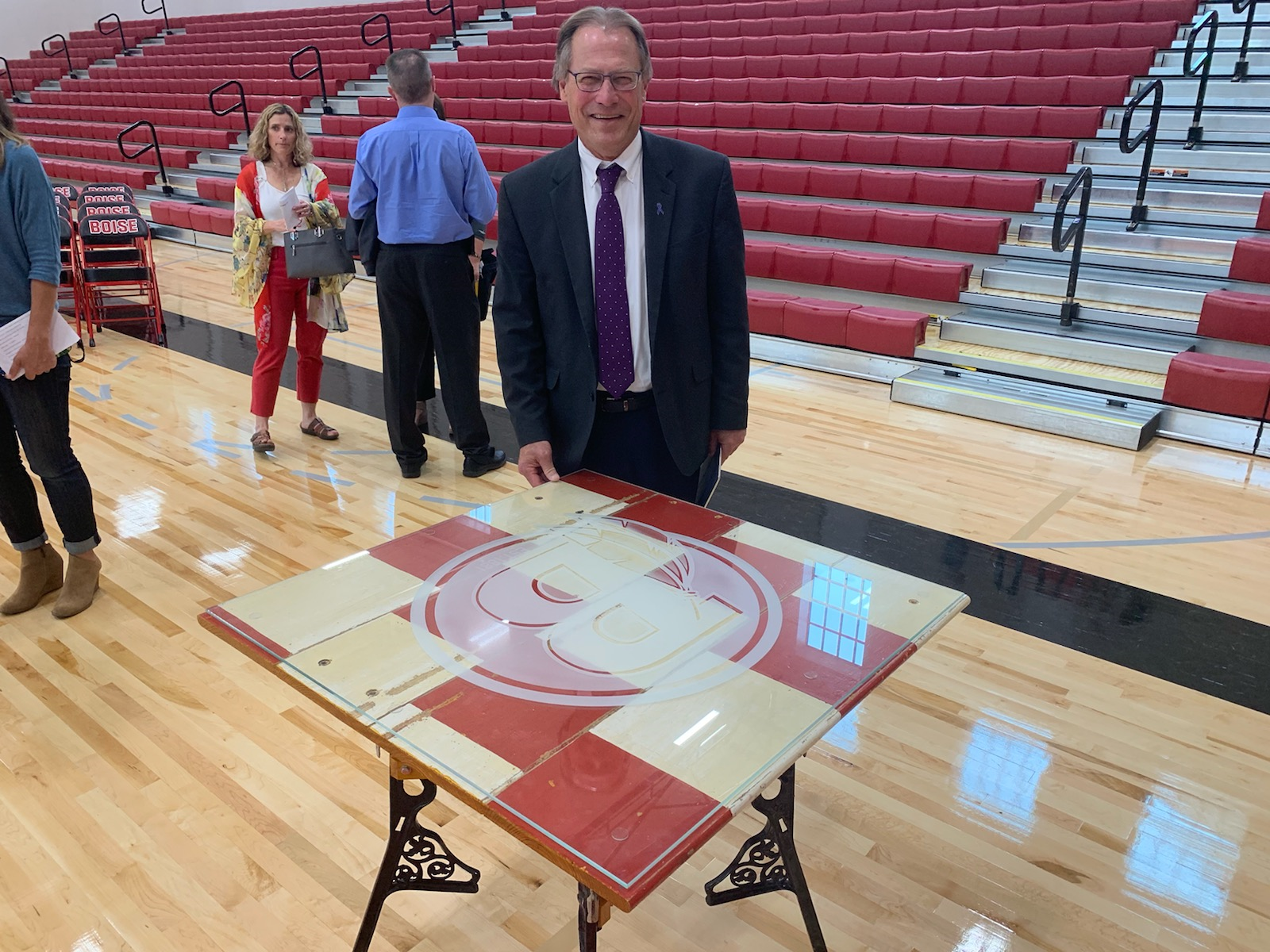 A man in a suit and tie is standing next to a table in a gym.