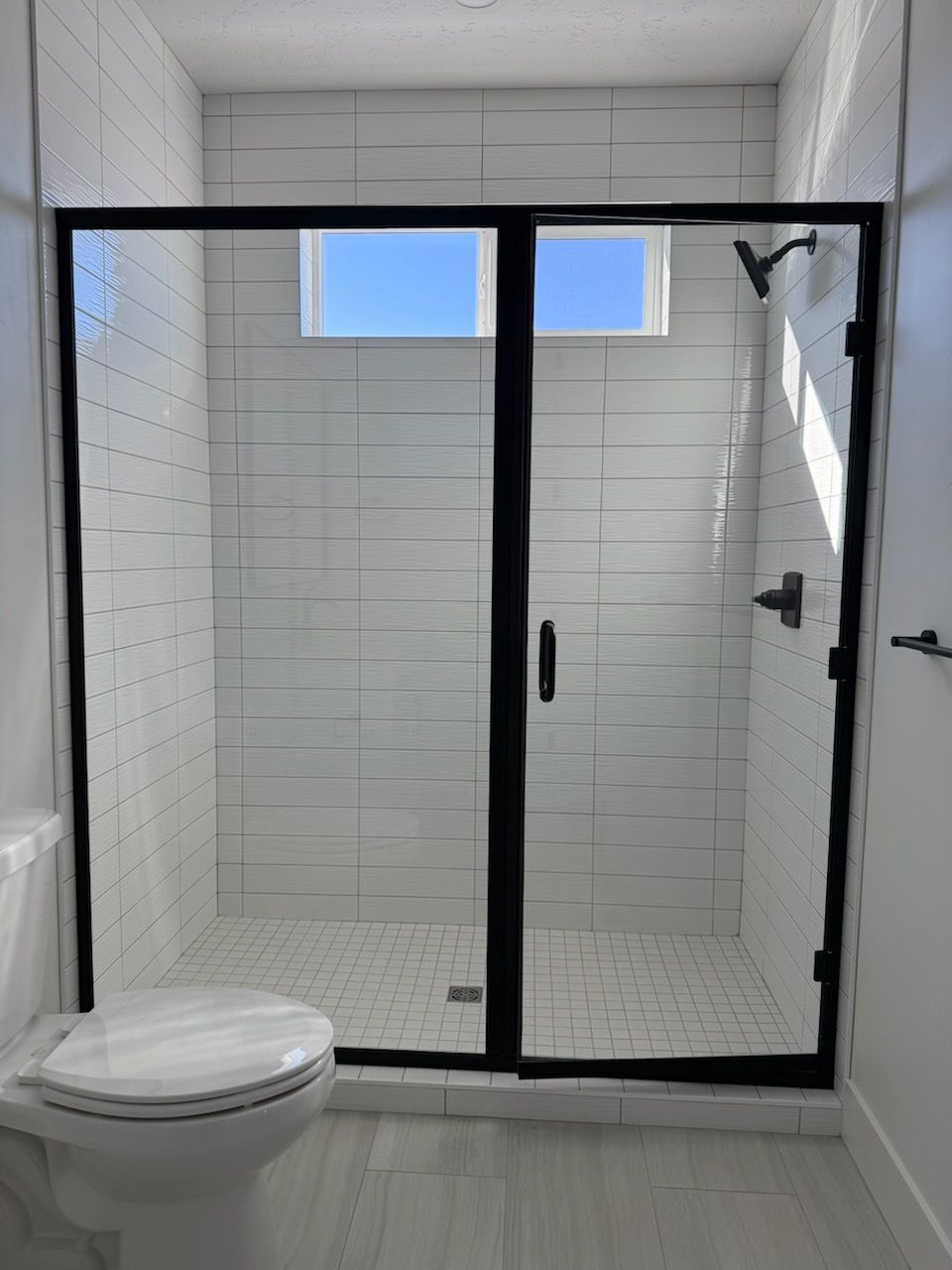 A bathroom with a toilet , shower , and window.