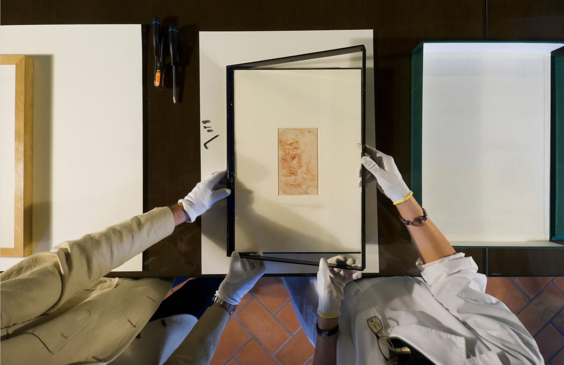 Two people are holding a framed picture on a table.