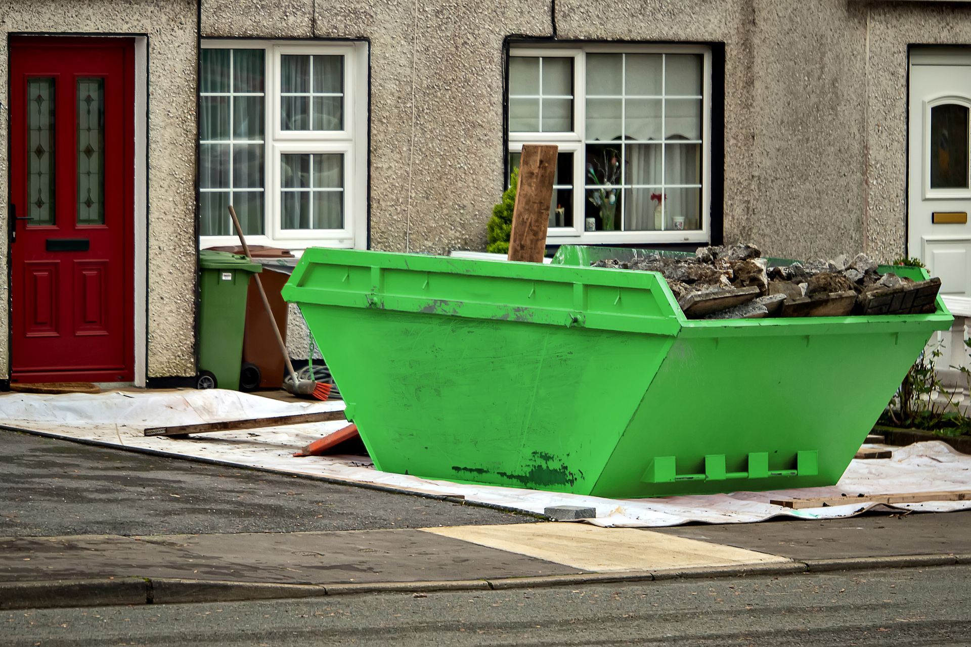 A green dumpster is in front of a house with a red door