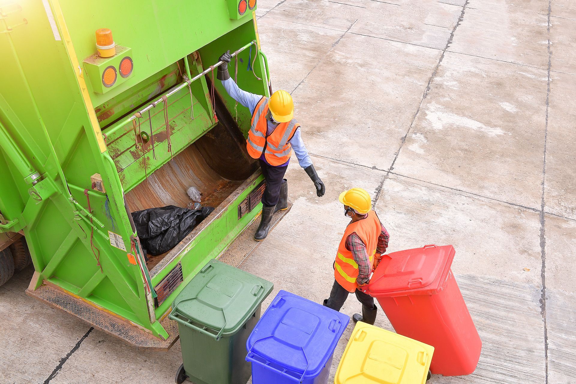 Two garbage workers are loading garbage into a garbage truck.