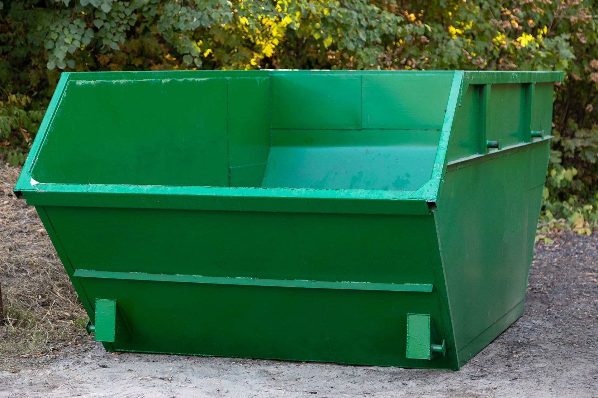 A green dumpster is sitting on top of a dirt field.