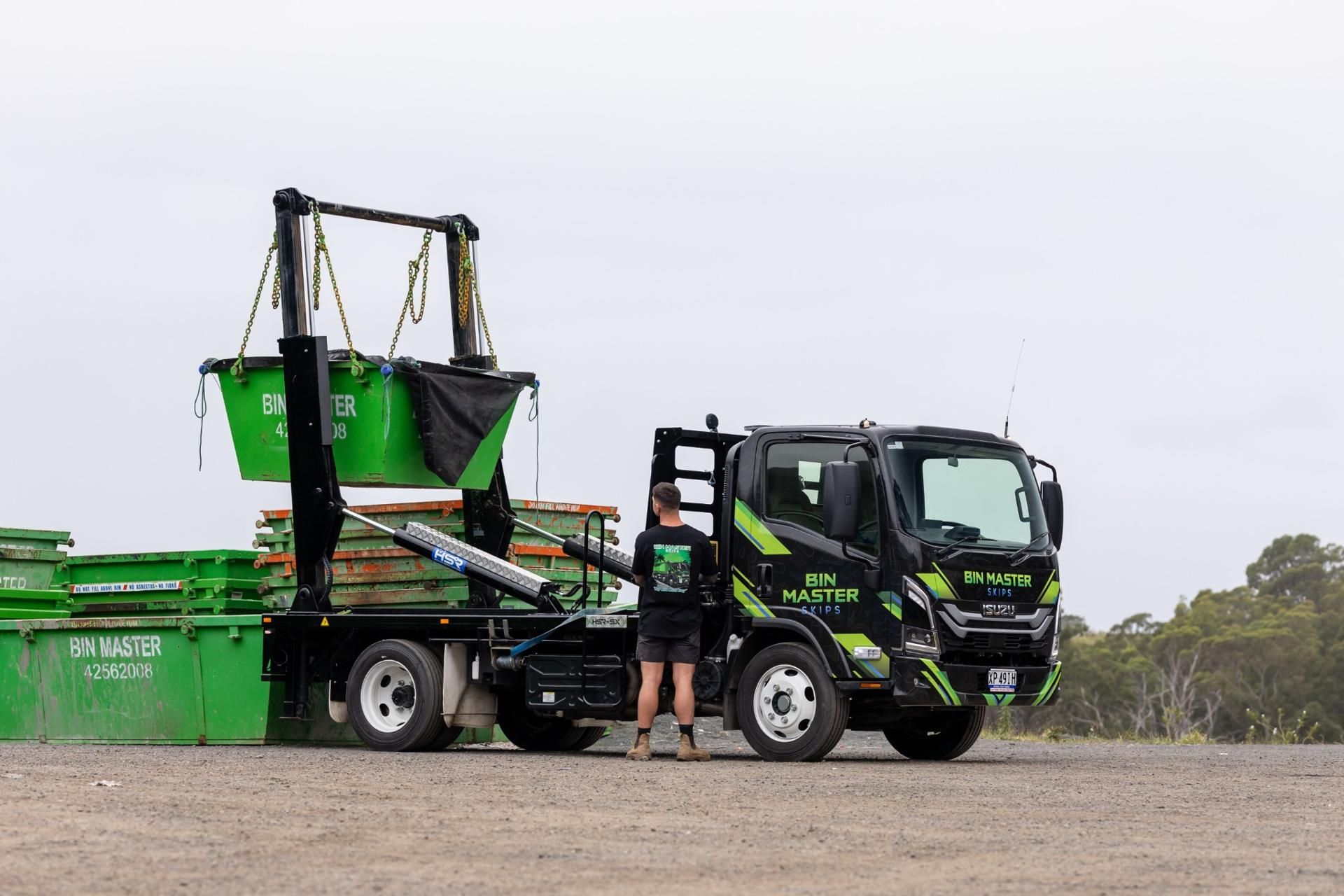Green dumpster filled with brick and construction debris in front of a red brick building.