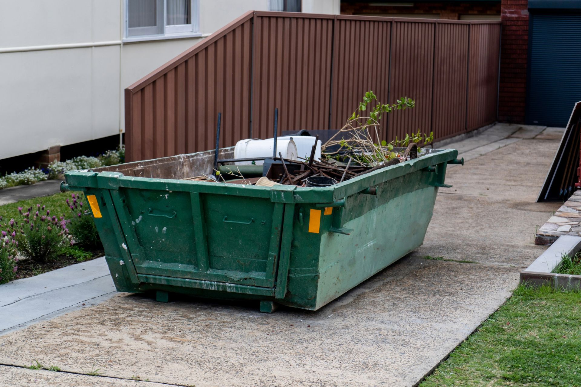 Green dumpster overflowing with debris on a concrete driveway.