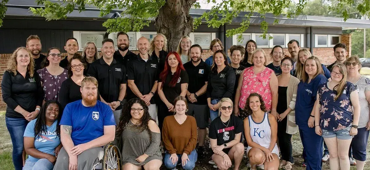 Group photo of diverse people posing outdoors in front of a tree.