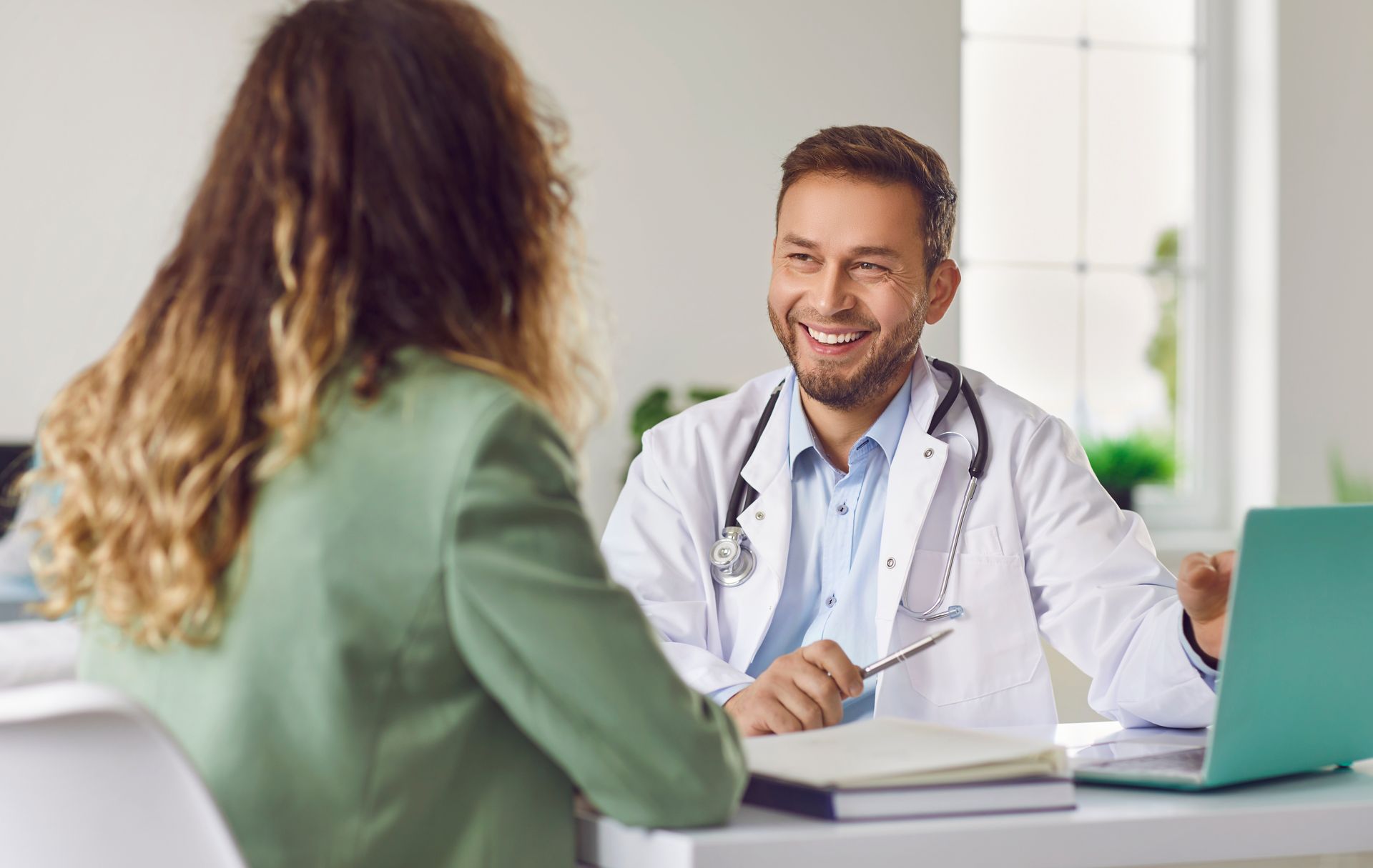 A smiling doctor in a lab coat with a stethoscope around his neck.