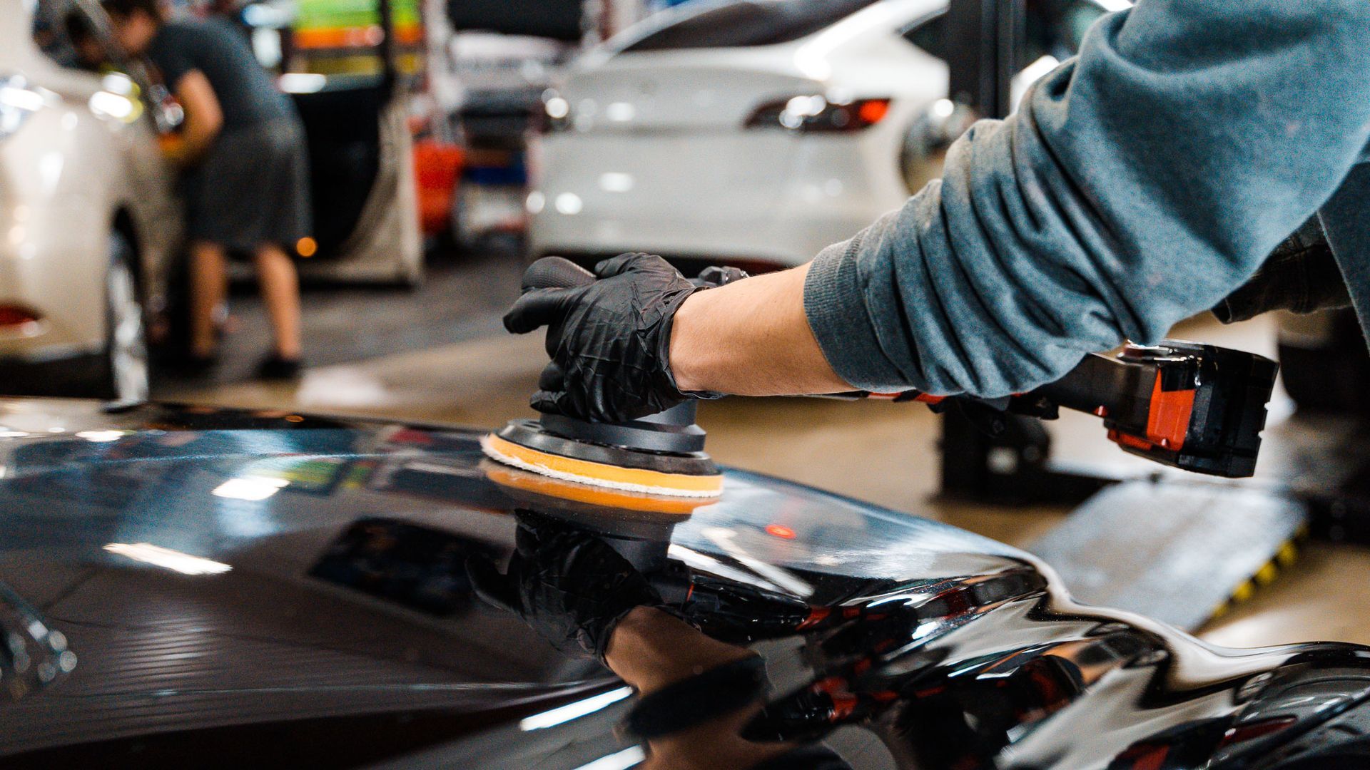 A person is polishing the hood of a car in a garage.
