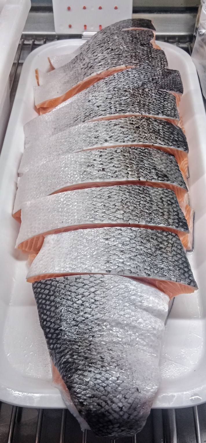 A whole salmon fillet, sliced into portions, arranged on a white foam tray inside a refrigerated display case.