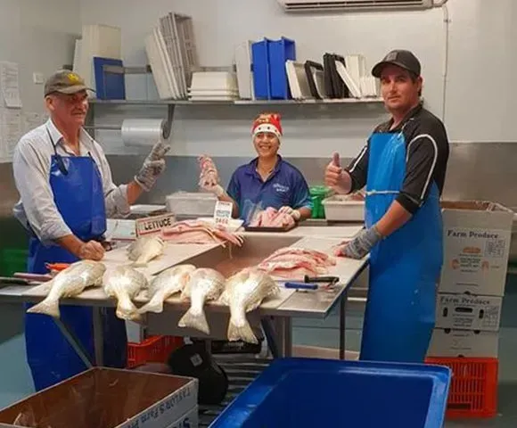 Three People in A Commercial Kitchen Preparing Fish at A Stainless Steel Table — Glenmore Seafoods In Park Avenue, QLD