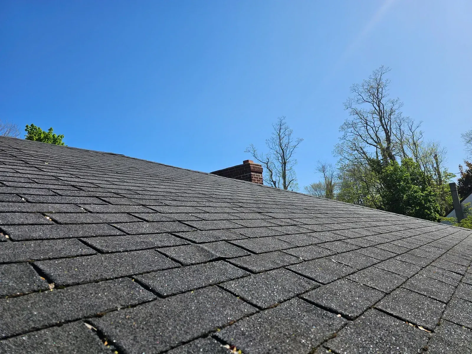 A close up of a roof with a chimney and trees in the background.