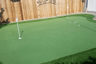 A backyard putting green with a wooden fence in the background.