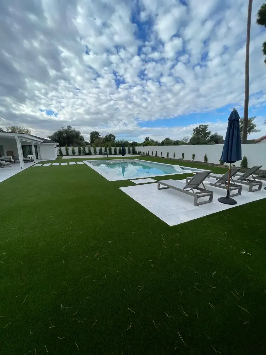 A large swimming pool surrounded by chairs and umbrellas in a backyard.