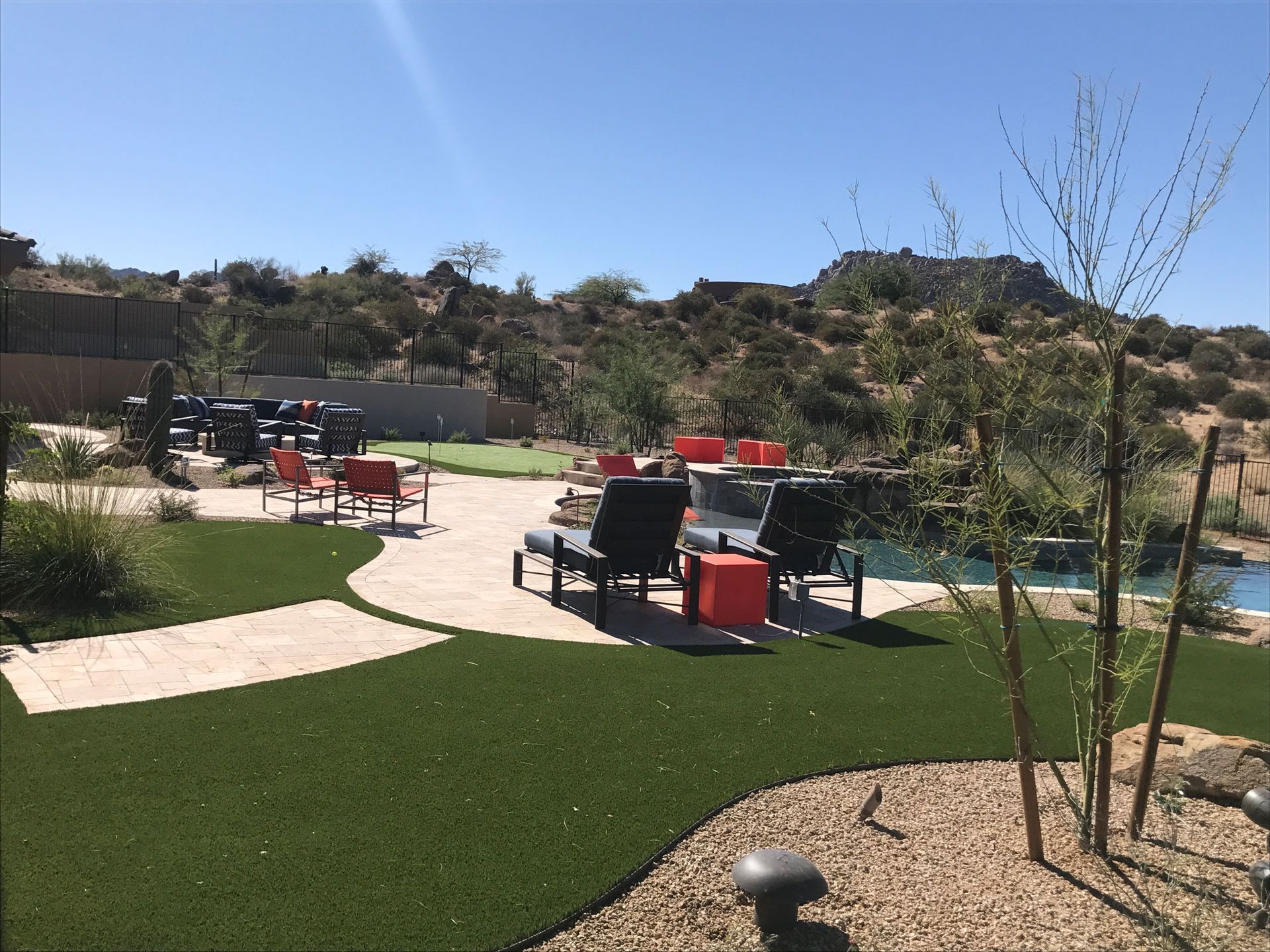 A backyard with a swimming pool and a patio area with chairs and tables.