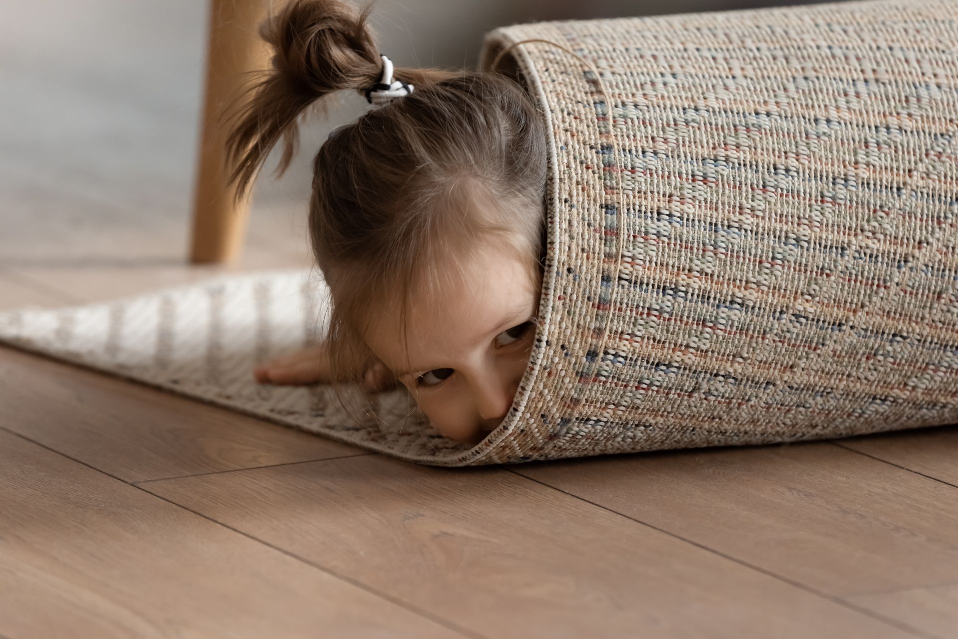 a little girl is sticking her head out of a roll of carpet .