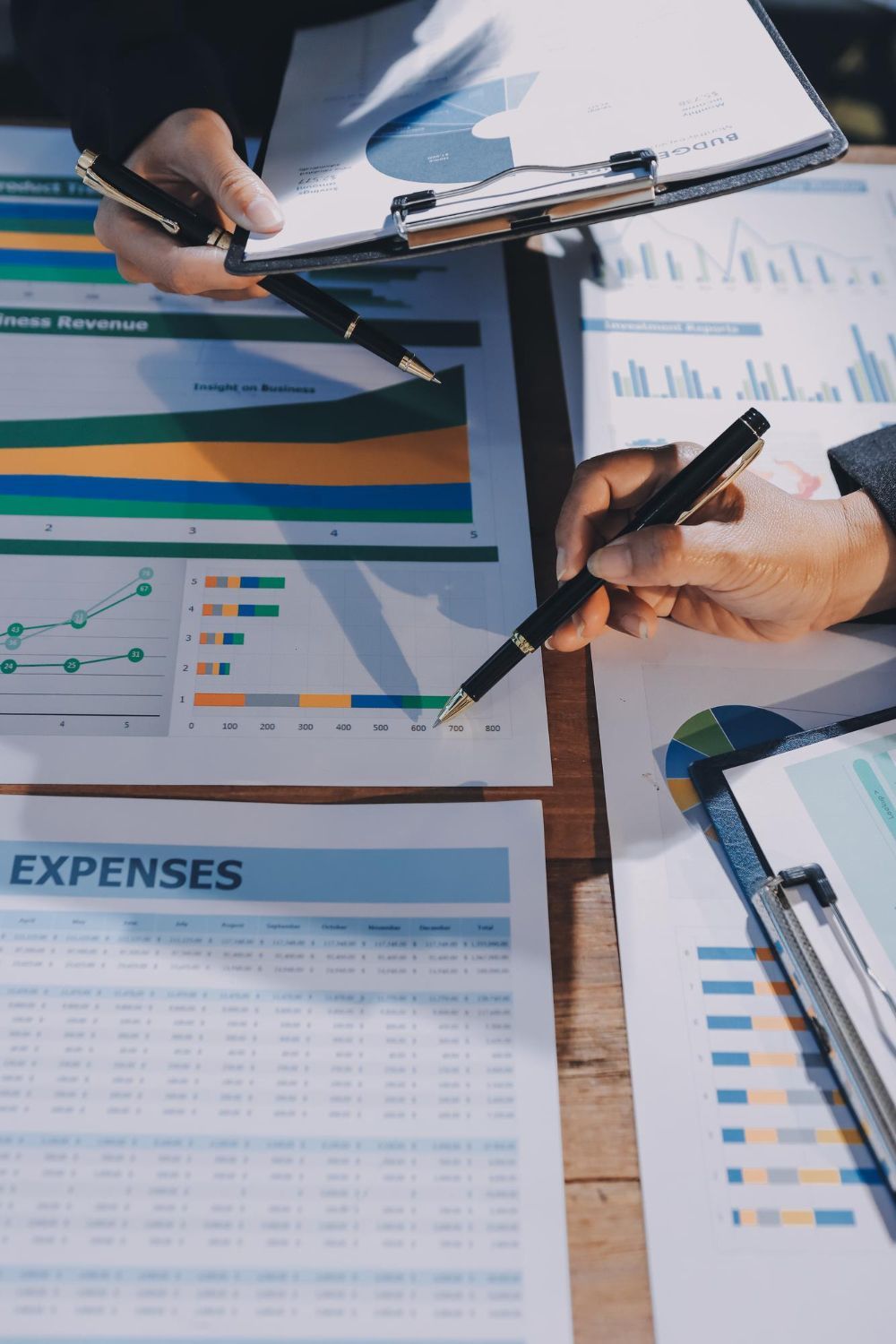 People reviewing financial reports with pens, charts, and spreadsheets on a table.