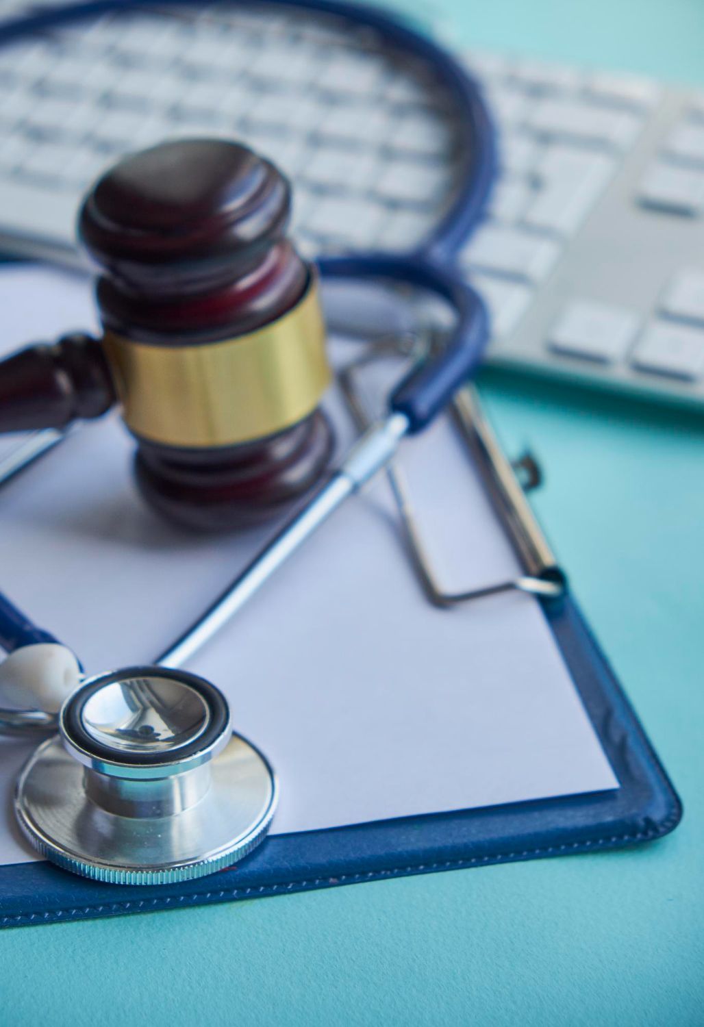 Gavel, stethoscope, and clipboard on a light blue surface, suggesting medical legal issues.