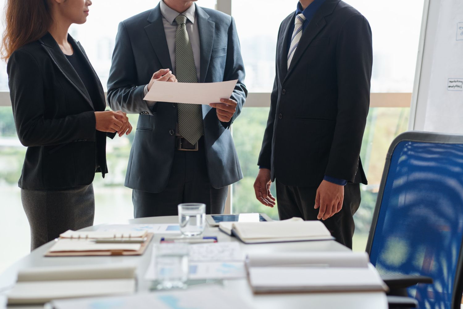 Three business people in suits reviewing documents at a conference table.