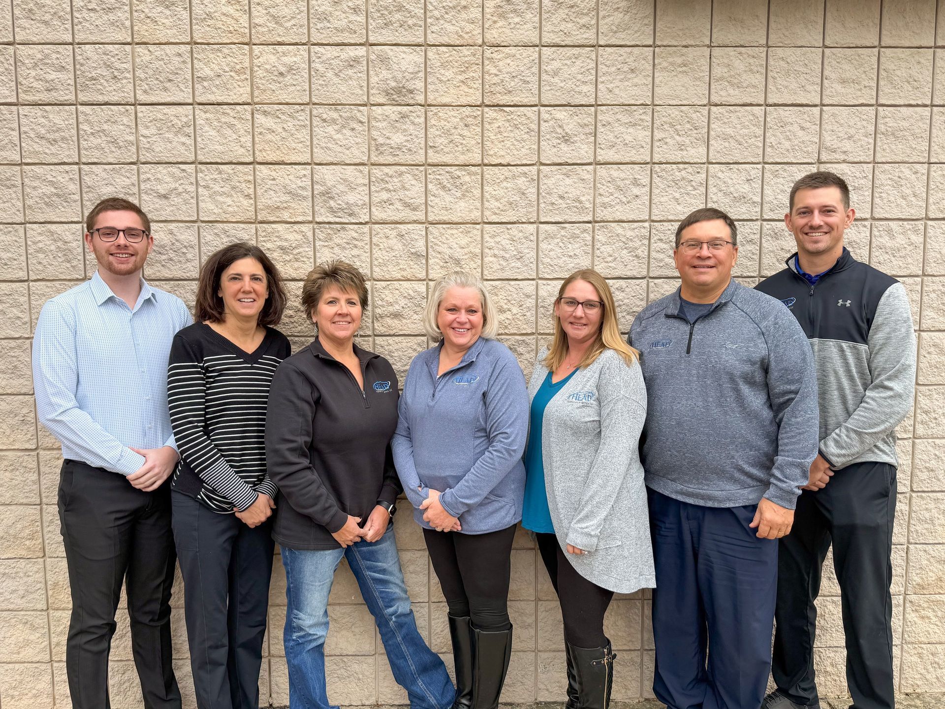 Woman in a black suit smiles while talking on a landline phone in an office setting.