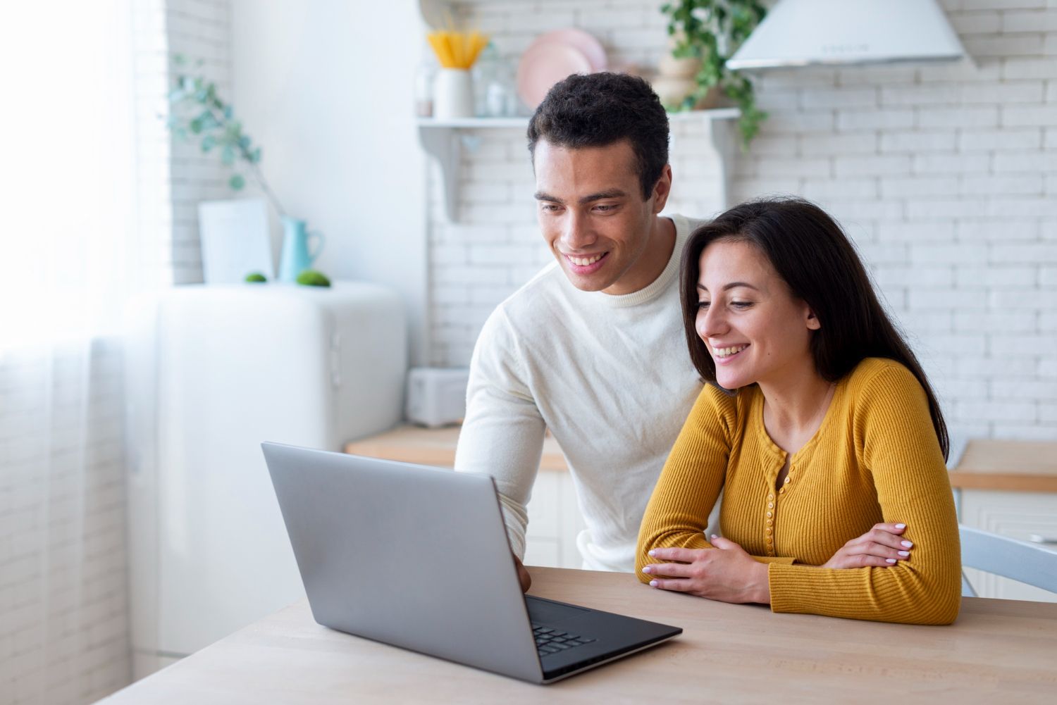 Couple smiling while looking at laptop screen in a kitchen.