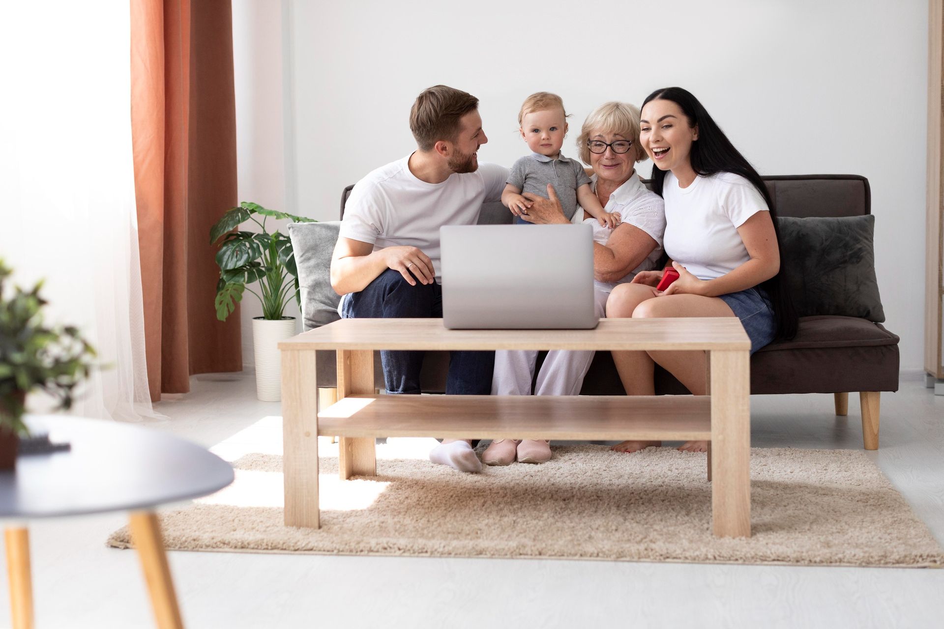 Family watching a laptop together on a couch; they are smiling and laughing.