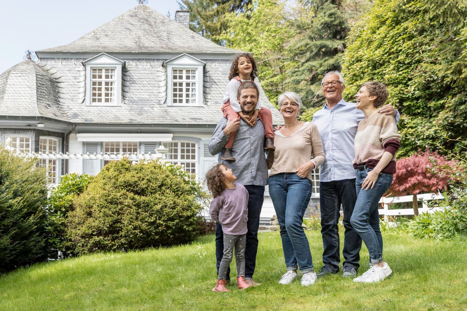 Family smiling in front of a house with a lush green lawn.