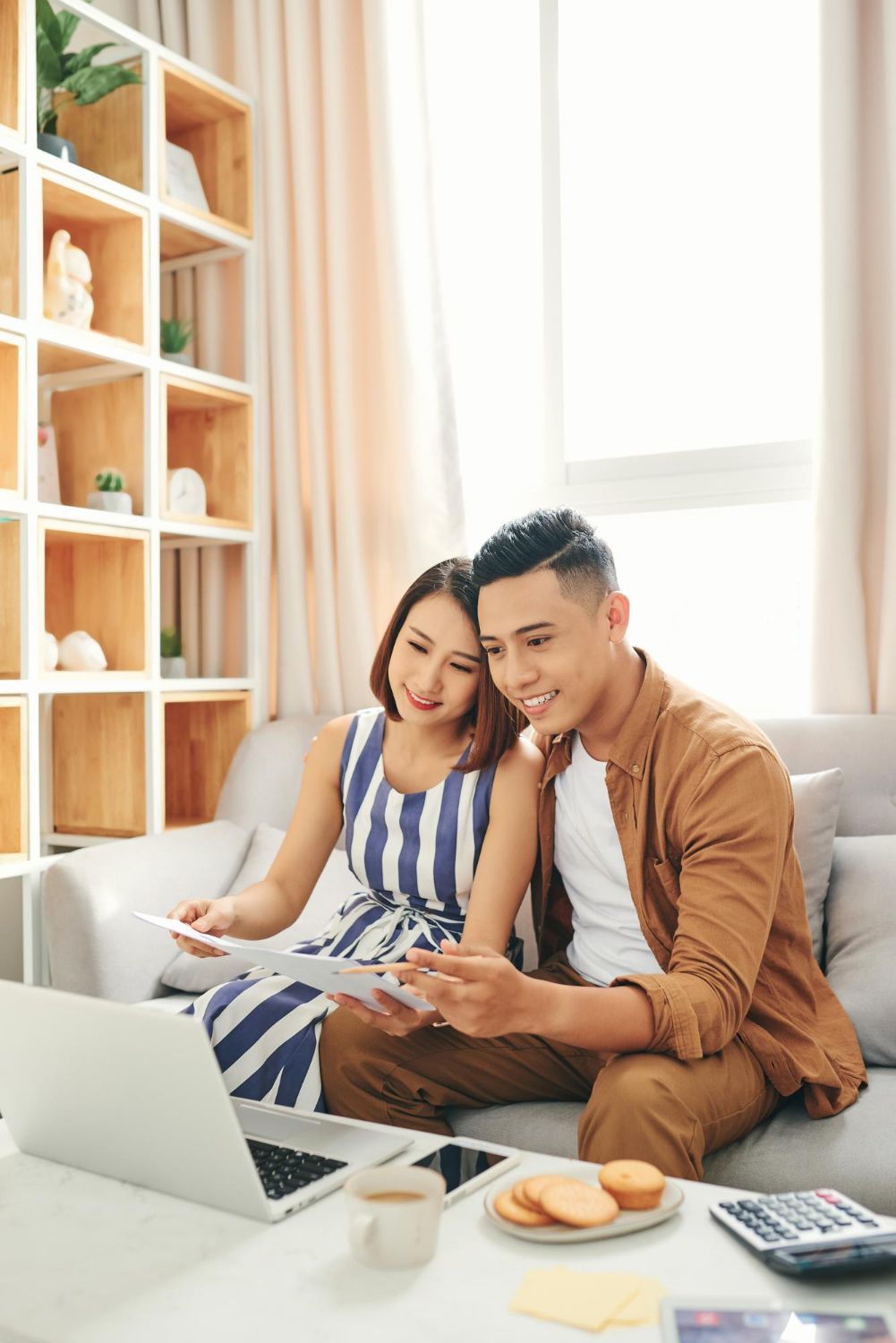 Couple on sofa looking at documents and laptop; living room setting.