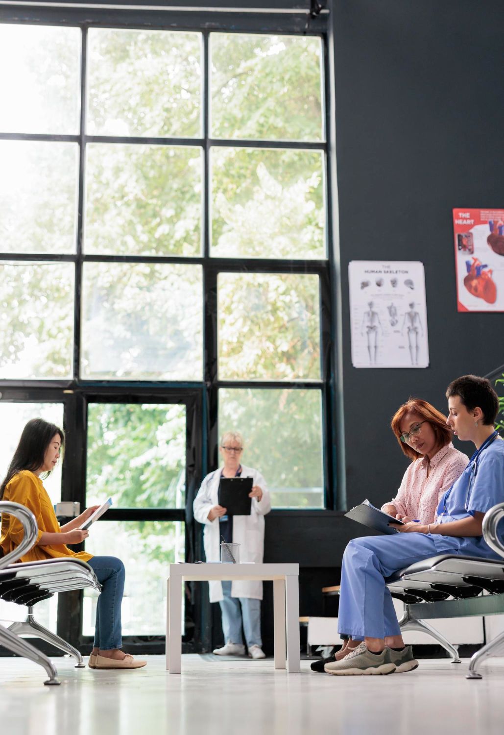 People in a waiting room. Doctor showing clipboard. Sunlight through large window.