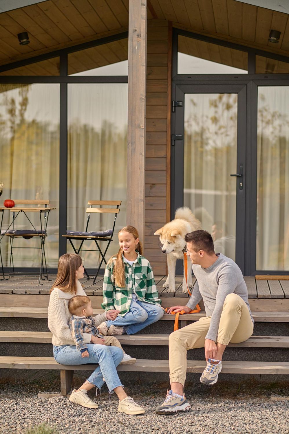 Family with dog on porch steps of wooden cabin; trees in the background.