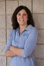 Woman in blue shirt with arms crossed, smiling in front of a textured wall.