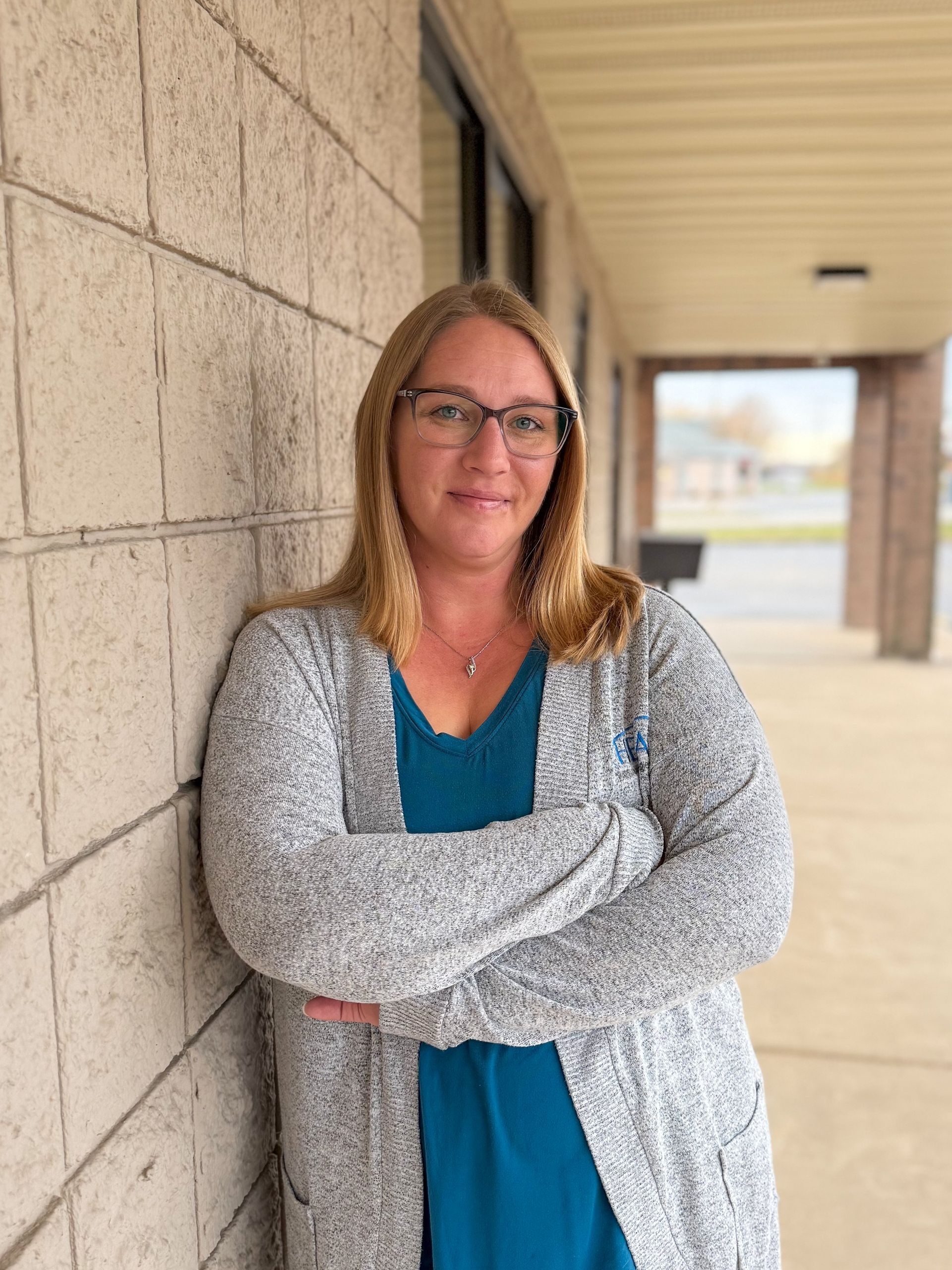 Woman with blonde hair wearing a floral top stands against a textured beige wall.