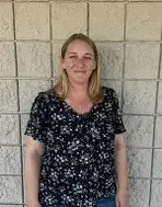 Woman with blonde hair wearing a floral top stands against a textured beige wall.